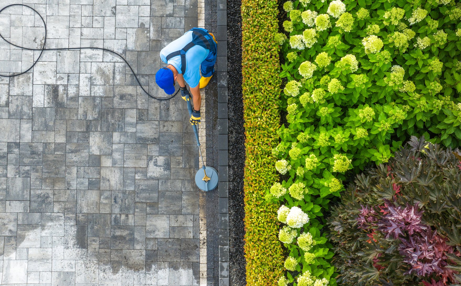 Worker with Pressure Washer Washing Residential Driveway Aerial View.